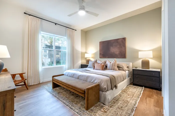 Inviting bedroom featuring a cozy bed, elegant decor, ample natural light, and polished wooden flooring.