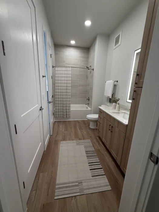 Elegant modern bathroom with sleek wood flooring, stylish vanity cabinet, and inviting bathtub with a subtle checkered shower curtain.