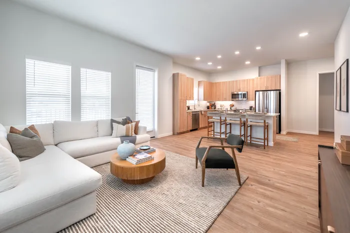 Modern open-concept living room with elegant kitchen, featuring sleek wooden floors, cozy sectional sofa, and stylish bar seating.