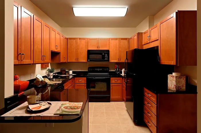 Warm and inviting kitchen with wooden cabinetry, black appliances, and granite countertops | Madison at Ballston Station | Arlington VA Apartments