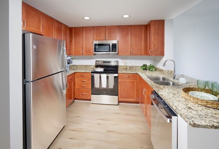 Newly renovated Ellington One Bedroom kitchen at Meridian at Grosvenor Station featuring sleek stainless steel appliances, modern vinyl plank wood-style flooring, and updated lighting fixtures that complement existing granite countertops and custom cabinetry | Newly Renovated Kitchen | Meridian at Grosvenor Station | North Bethesda MD Apartments | Rockville MD Apartments