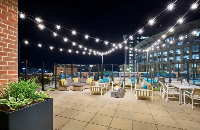 Outdoor resident lounge at Meridian at Eisenhower Station featuring a fire pit, string lights, and multiple modern seating areas. | Luxury Alexandria VA Apartments