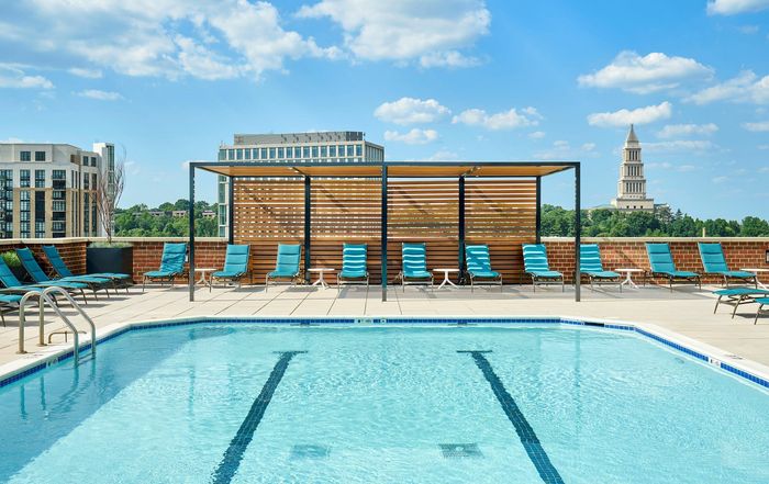 Renovated swimming pool area with a shade trellis, lounge chairs, and patio tables at Meridian at Eisenhower Station. | Luxury Alexandria VA Apartments