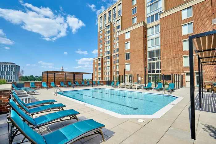 Renovated swimming pool area with a shade trellis, lounge chairs, and patio tables at Meridian at Eisenhower Station. | Luxury Alexandria VA Apartments