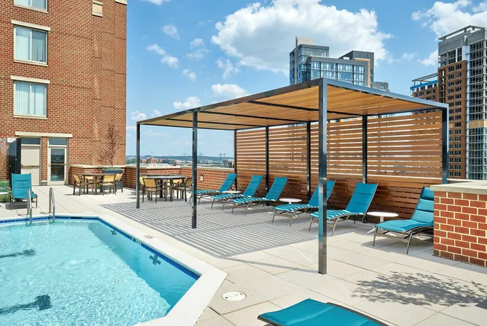 Renovated swimming pool area with a shade trellis, lounge chairs, and patio tables at Meridian at Eisenhower Station. | Luxury Alexandria VA Apartments