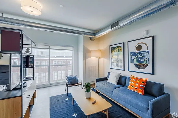 Contemporary living room with chic blue sofa, large windows, modern art, and stylish exposed ductwork.