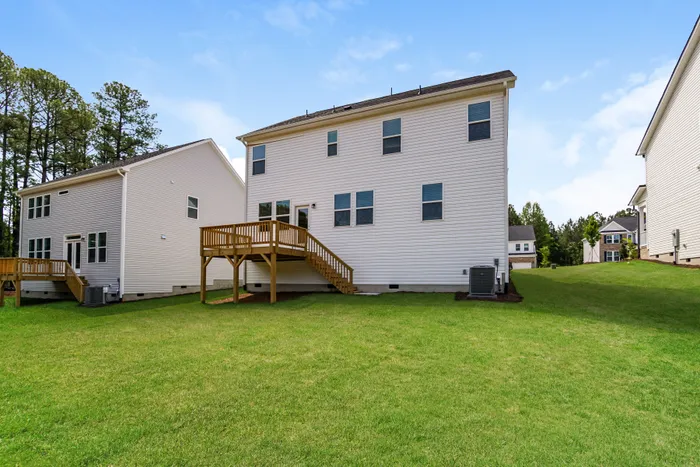Charming suburban home with a spacious deck, nestled in a lush green lawn and surrounded by serene trees.