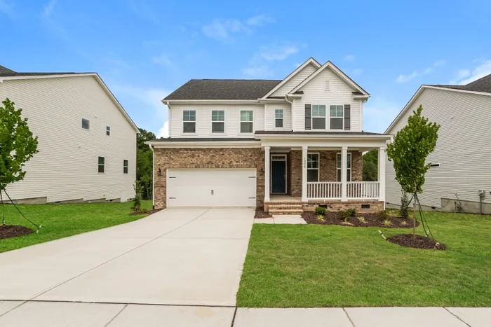 Charming suburban two-story home with brick facade and white accents, featuring a spacious front porch and lush green lawn.