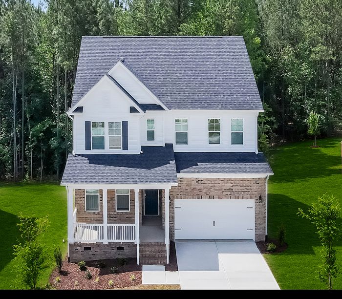 Charming two-story suburban home with a welcoming front porch, surrounded by lush greenery and featuring a spacious driveway.