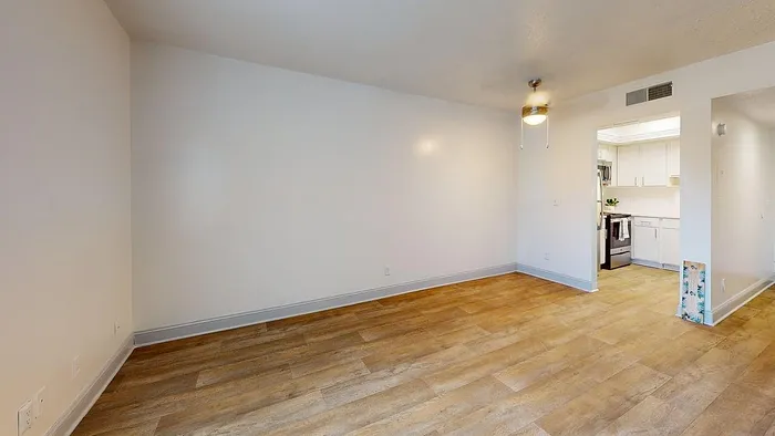 Inviting open-concept living and dining area with elegant wood flooring, bright walls, and a modern ceiling fan, leading to a sleek kitchen.