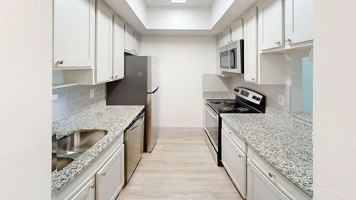 Modern kitchen with granite countertops, white cabinetry, stainless steel appliances, and sleek wooden flooring.