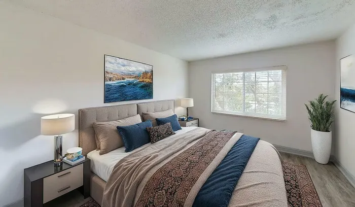 Bright and cozy bedroom with elegant decor, featuring a plush king-sized bed, stylish side tables with lamps, large window for natural light, and serene artwork.