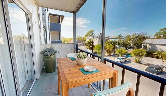 Charming balcony with a cozy wooden dining table, lush greenery, and an inviting view of a sunny neighborhood.