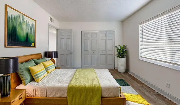 Bright and inviting bedroom with modern decor, featuring a plush bed, stylish artwork, and ample natural light from large window blinds.