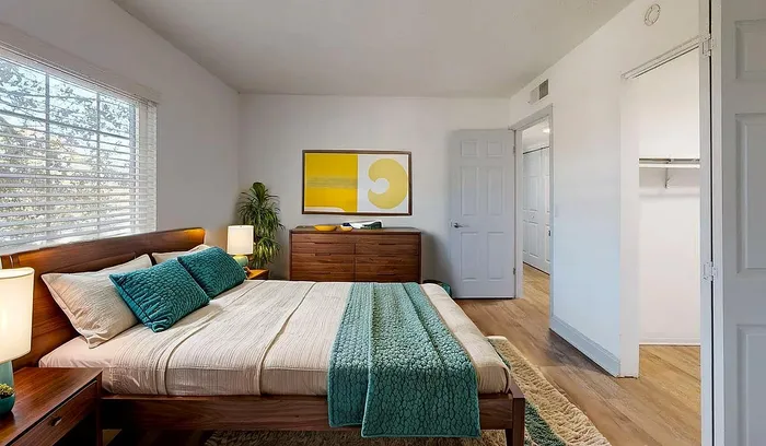 Inviting bedroom with modern decor, featuring a cozy wooden bed, vibrant teal accents, and a large closet. Sunlit space offers a serene and stylish retreat.