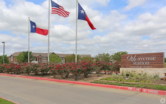 Entrance of 9th Avenue Station Apartment Homes with flags and blooming flowers.