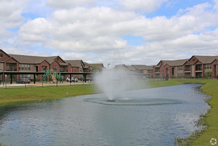 Scenic apartment complex with fountain, playground, and lush greenery.