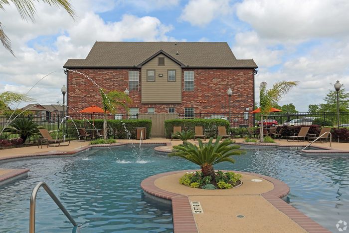 Charming brick apartment building with a luxurious swimming pool surrounded by sun loungers and vibrant greenery.