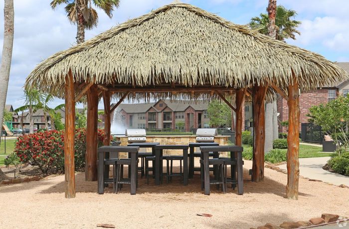 Tropical-themed outdoor BBQ area with wooden pergola and modern grills surrounded by lush landscaping.