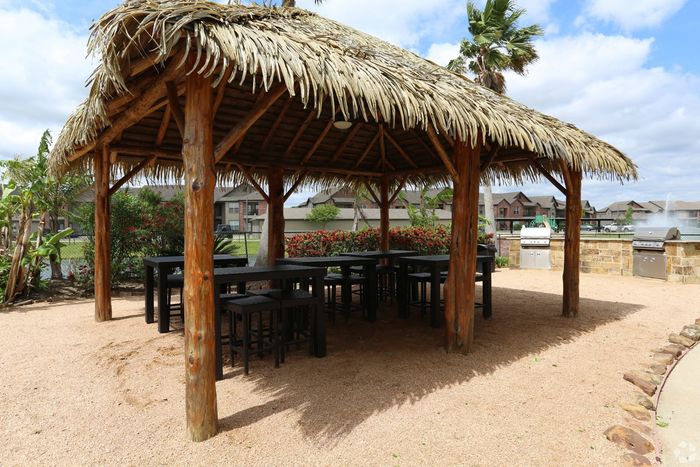 Charming tropical outdoor area with a thatched-roof gazebo, seating, and grilling stations.
