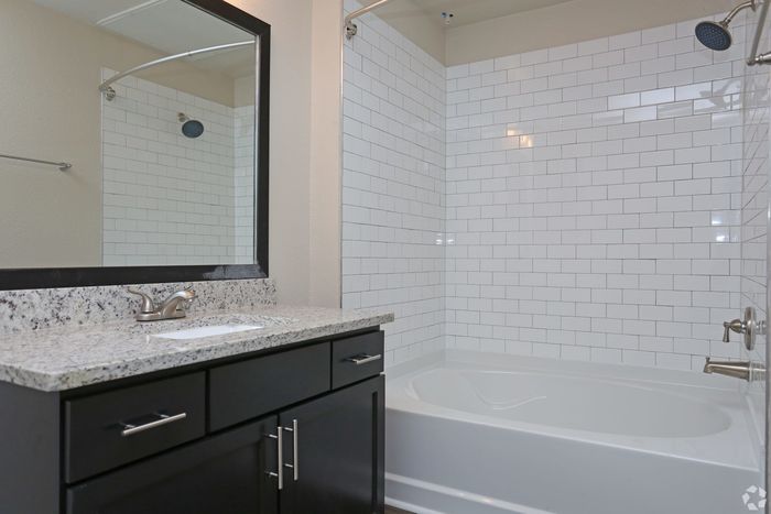 Sleek bathroom with a granite countertop, large mirror, and white subway tile shower.