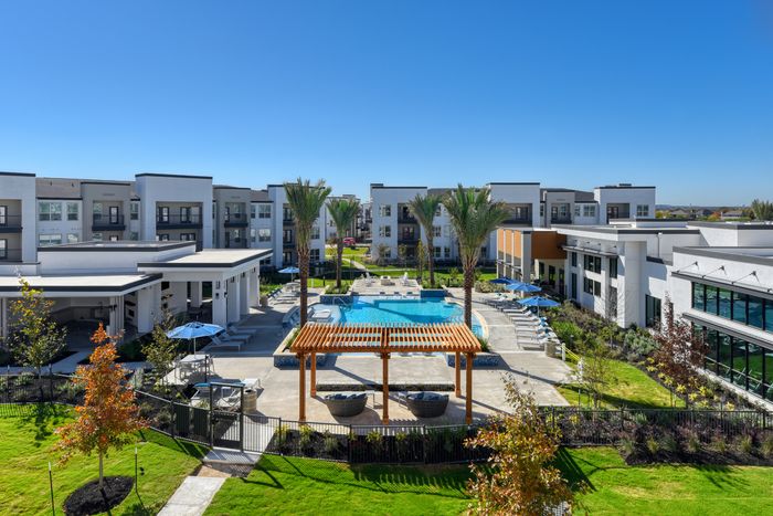 Luxurious apartment complex featuring a central pool, lush greenery, and modern architecture under a bright blue sky.