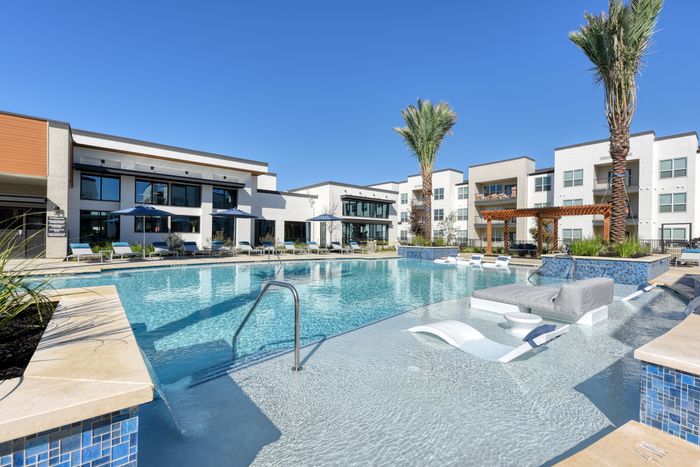 Luxurious apartment complex with a stunning swimming pool featuring sun loungers, palm trees, and modern architectural design.