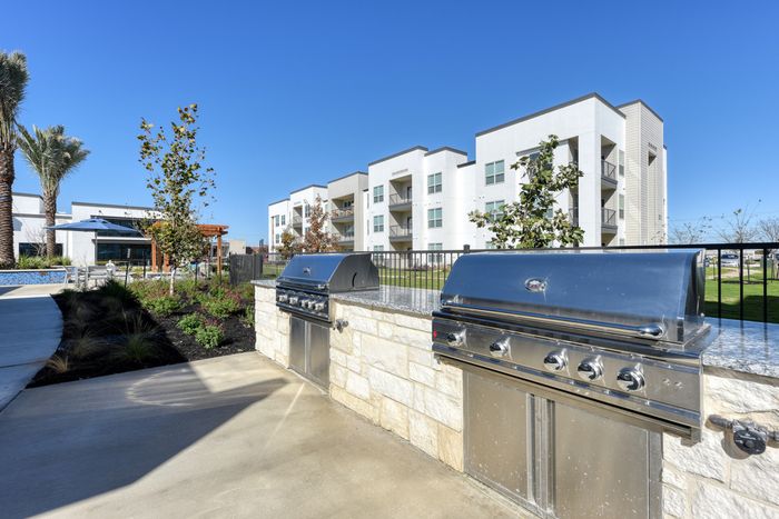 Modern apartment complex with outdoor stainless steel grills and lush landscaping, perfect for social gatherings and relaxation.