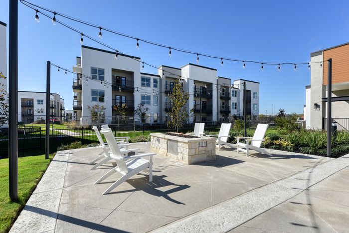 Elegant outdoor patio area with cozy seating and a fire pit, surrounded by modern apartment buildings under a clear blue sky.