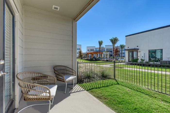 Charming patio view with stylish wicker chairs overlooking beautifully landscaped grounds and modern apartment architecture.