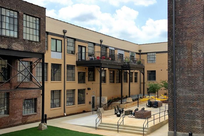Charming brick apartment complex with spacious outdoor patio, featuring modern railing and vibrant seating areas under a bright sky.