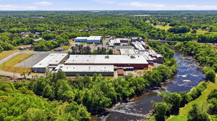 Expansive aerial view of a picturesque industrial complex surrounded by lush greenery and a tranquil river, offering a unique natural setting.