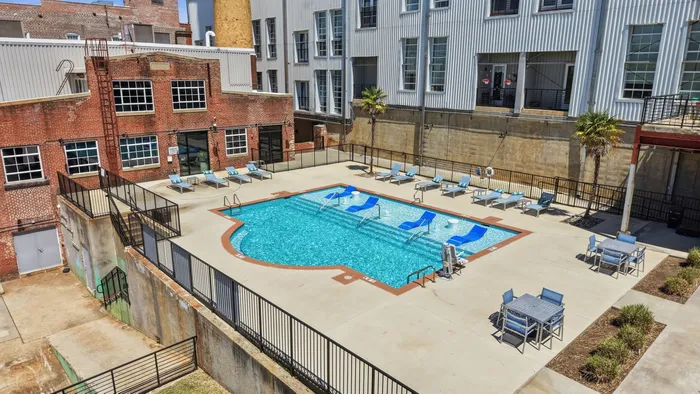 Chic urban apartment complex with a sparkling outdoor pool, surrounded by stylish lounge chairs and modern industrial architecture.