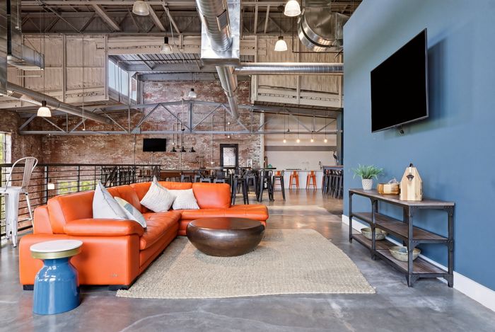 Modern industrial loft with vibrant orange couch, sleek open kitchen, and stylish decor enhancing a spacious living area.