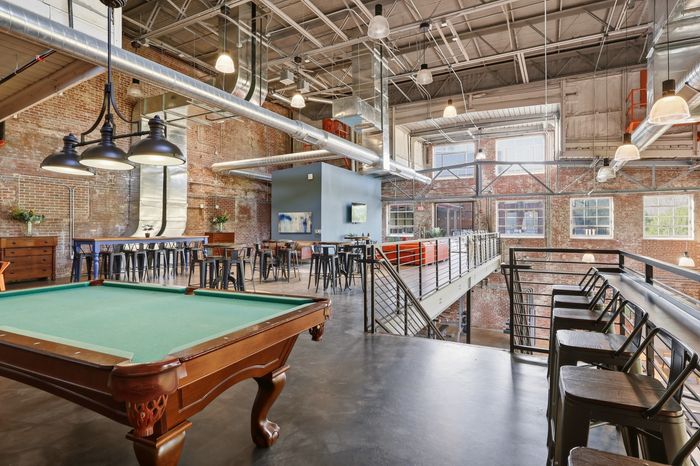 Chic loft-style common area with exposed brick walls, large industrial windows, and a pool table, perfect for modern urban living.