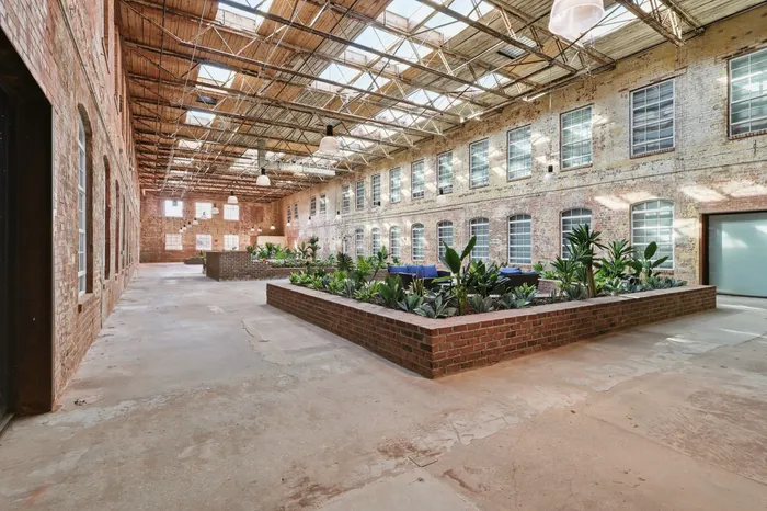 Spacious industrial-style atrium with exposed brick walls, skylight ceiling, and lush indoor garden.
