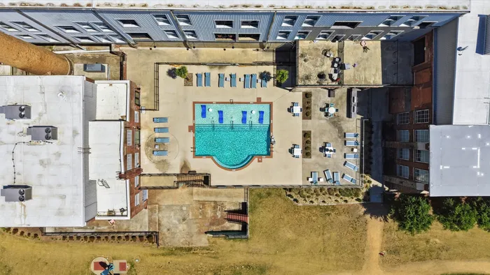 Aerial view of a luxurious apartment complex featuring a sparkling pool surrounded by elegant lounge chairs and modern buildings.