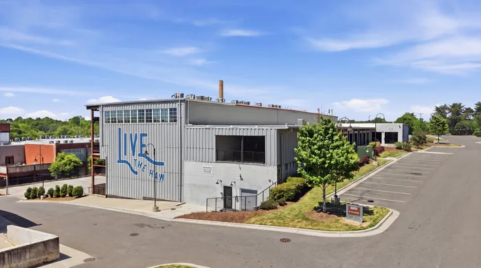 Modern industrial building with 'Live The Haw' signage, surrounded by lush greenery and ample parking space on a sunny day.
