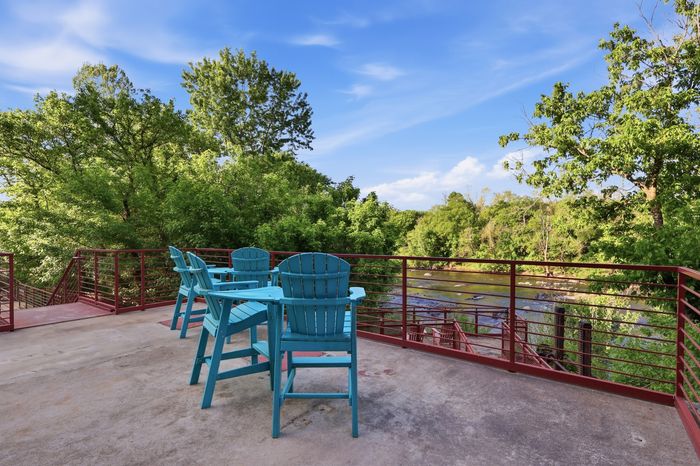 Inviting outdoor patio with vibrant blue seating, overlooking lush green trees and a tranquil river, perfect for relaxation and scenic views.