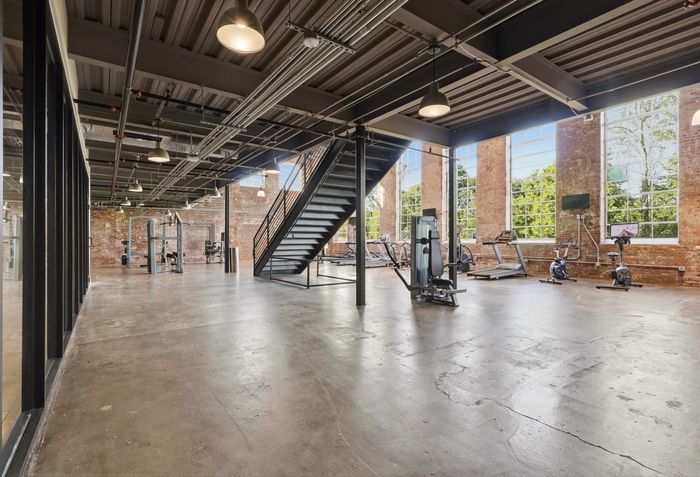 Spacious industrial-style gym with state-of-the-art equipment, large windows, and modern design elements.