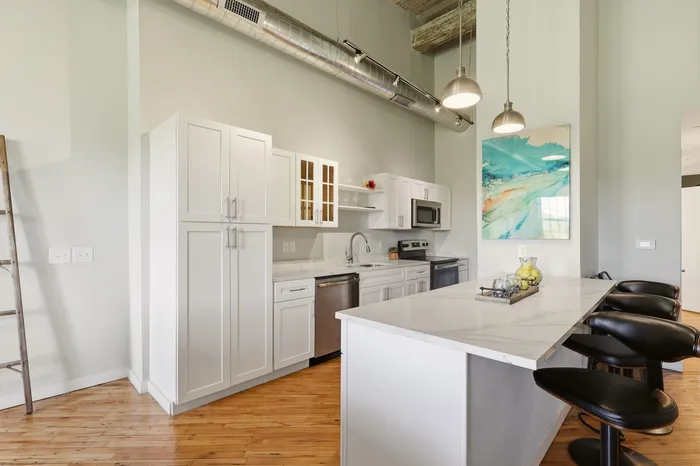 Modern kitchen with sleek white cabinets, marble countertops, and stainless steel appliances, featuring a stylish island with bar seating and artistic decor.