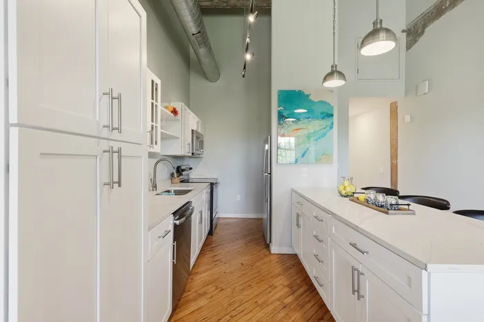 Chic modern kitchen with sleek white cabinetry, elegant countertop, and stylish pendant lighting, featuring stainless steel appliances and artistic decor.