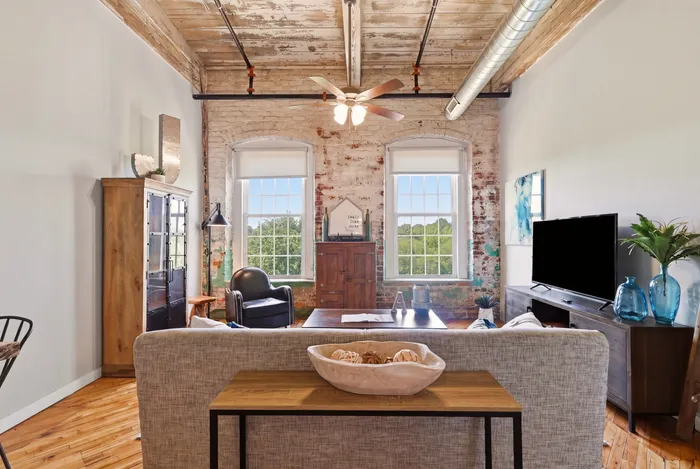 Charming loft-style living room with exposed brick walls, large windows, and stylish rustic decor.