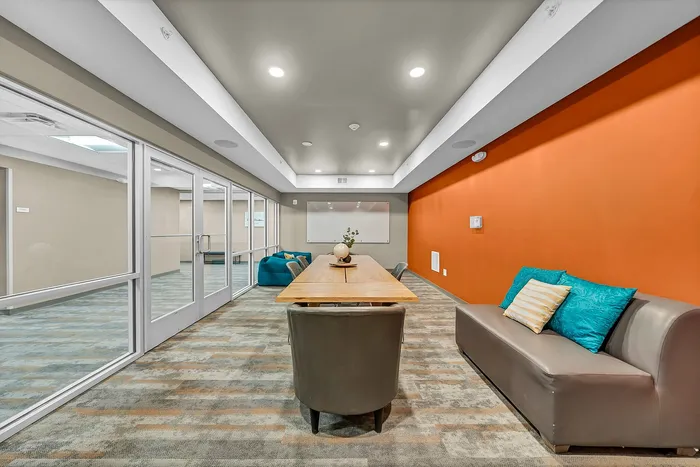 Contemporary meeting room with a vibrant orange accent wall, stylish seating, and a sleek wooden table, perfect for collaboration, studying, and productivity.