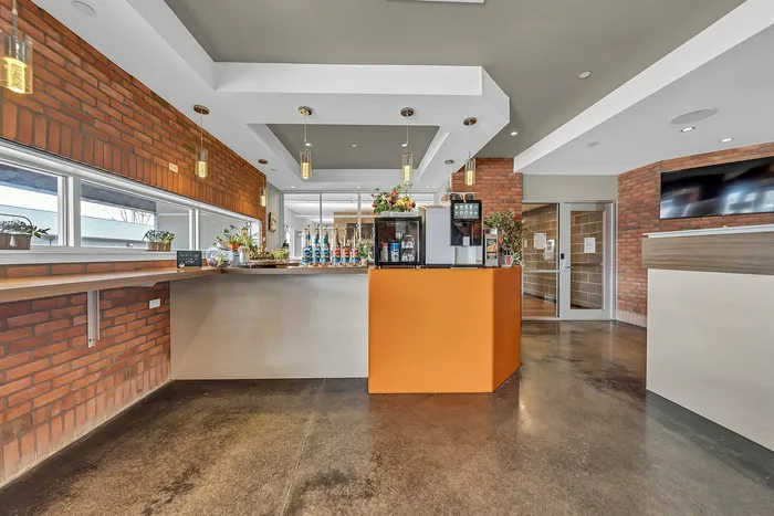 Inviting coffee bar with free coffee, modern decor, featuring warm brick accents, sleek orange counter, and ample natural light.