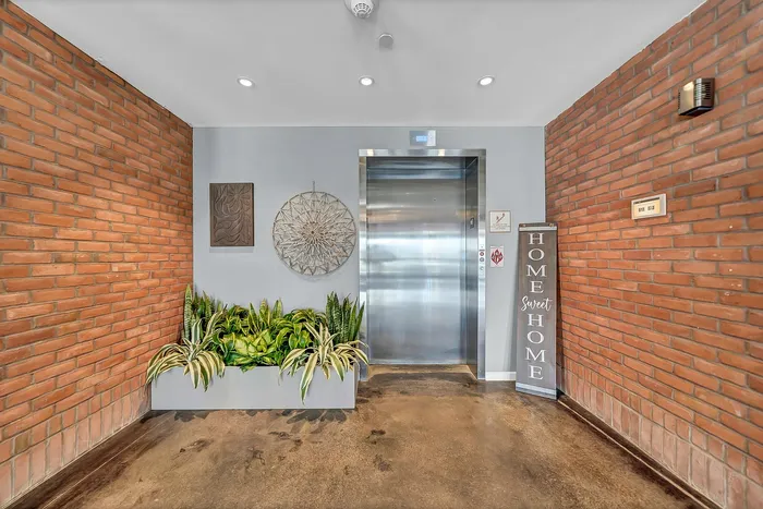 Inviting apartment lobby with modern elevator, vibrant indoor plants, and stylish decor against rustic brick walls. Home sweet home sign.