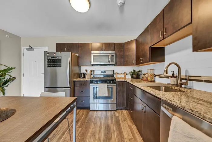 Modern kitchen in apartment complex with sleek stainless steel appliances, dark wood cabinets, and granite countertops.