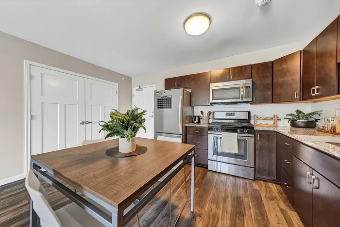 2 bedroom apartment full kitchen with dark wood cabinets, stainless steel appliances, and a cozy dining area with a stylish wooden table, enhanced by natural light and polished wooden floors.