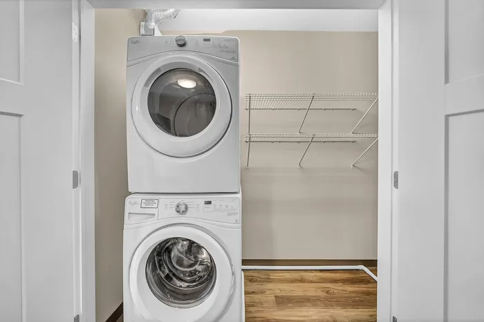 In-unit laundry space with stacked washer and dryer, energy efficient appliances, with a large closet featuring shelving and storage.