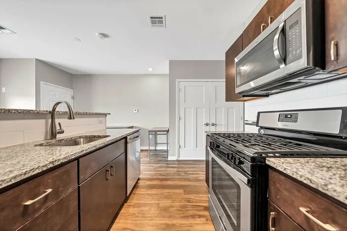 Studio apartment full kitchen with granite countertops, stainless steel appliances, energy efficient appliances, and elegant wood flooring, offering a stylish and functional apartment living space.